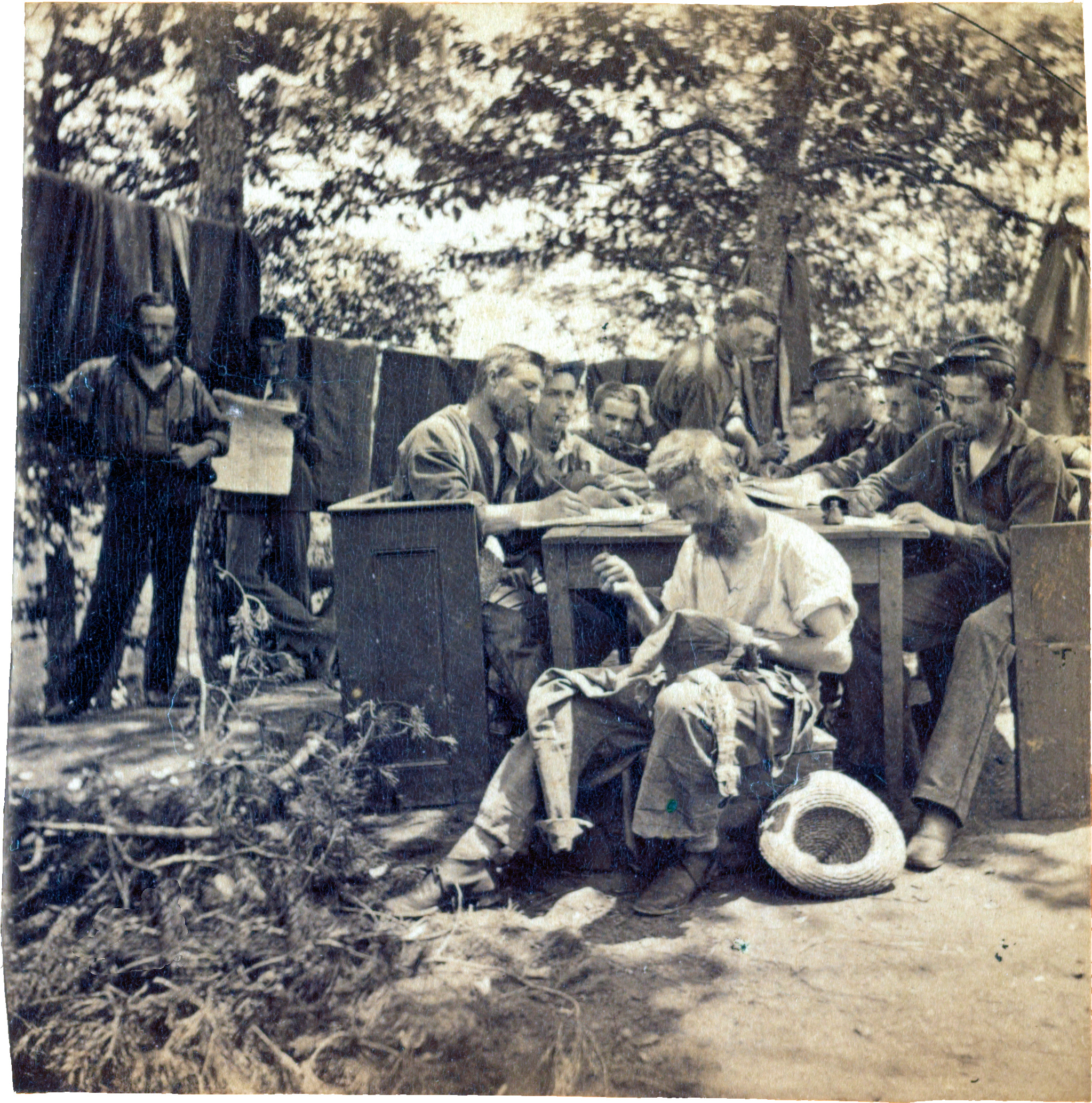 Boston Light Artillery soldiers in camp at Relay House in Maryland sitting at a long table, writing letters, as one soldier, in the foreground, appears to be sewing.
